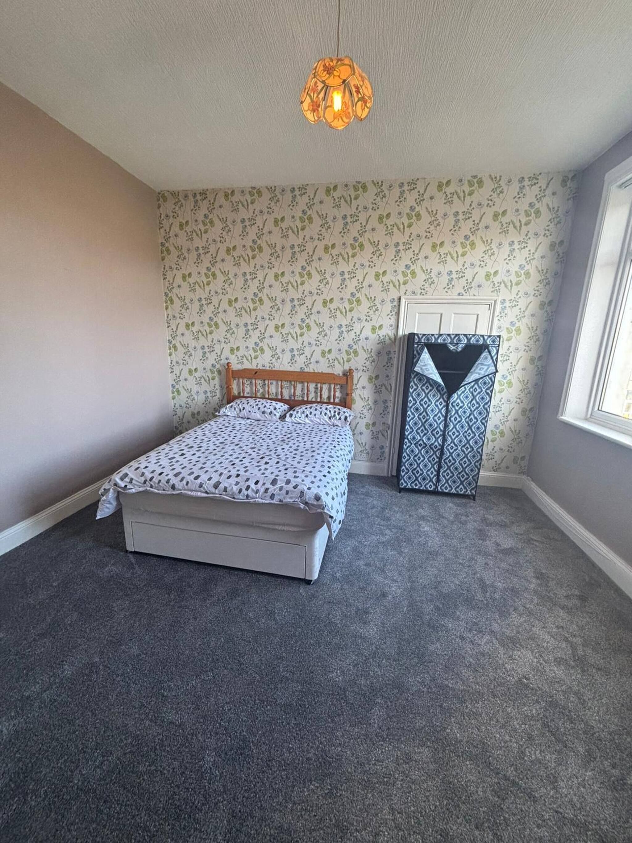 Une chambre à coucher comprenant un lit, une armoire, un tapis à motifs et un papier peint à fleurs.