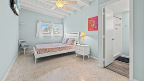 A bedroom with a bed, a nightstand, a chair, a ceiling fan, and a door leading to a bathroom. - Beautiful 2-bedroom house with Dock in Key Colony Beach (Key Colony Beach)