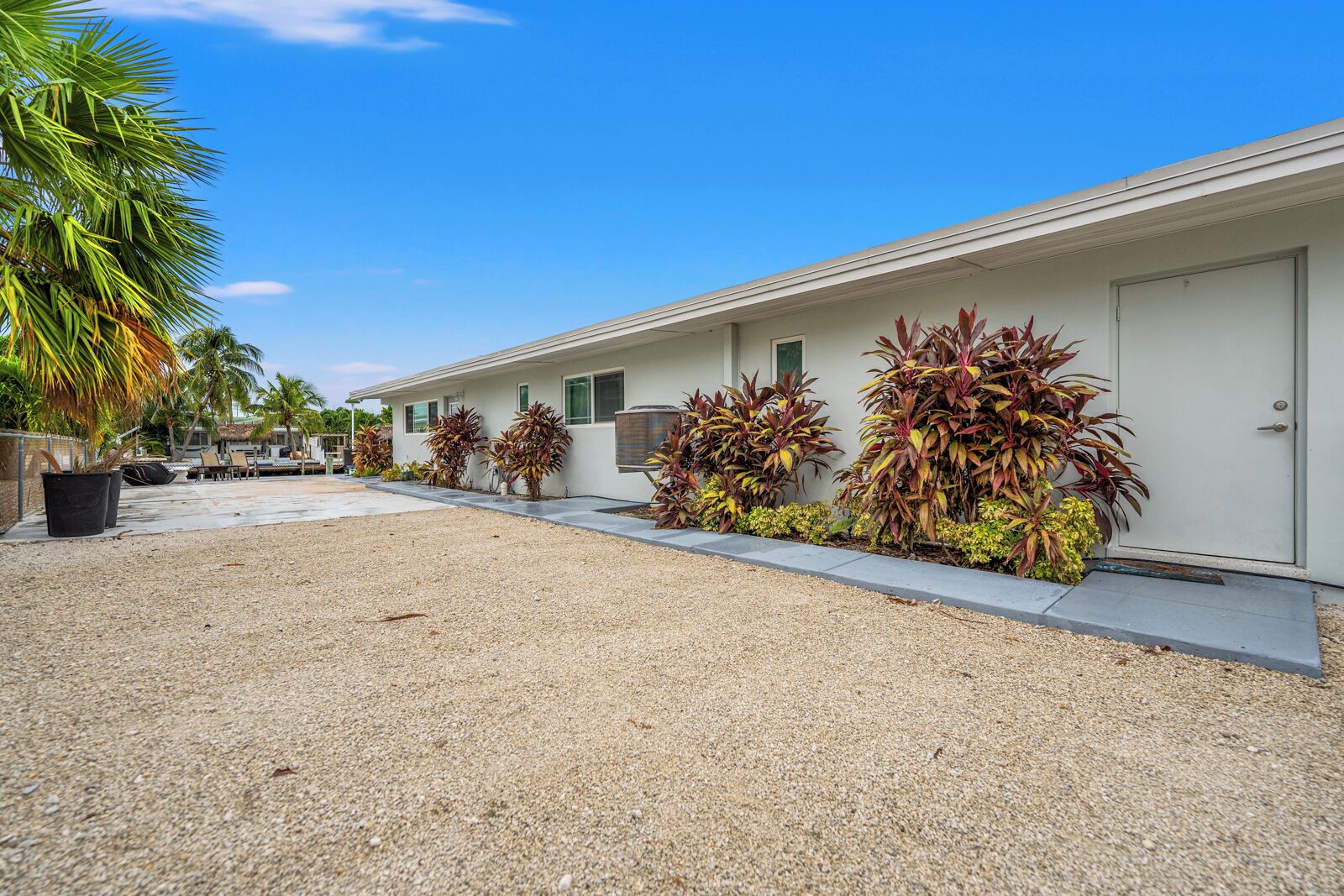A row of motel rooms with a gravel driveway, palm trees, and a clear blue sky.