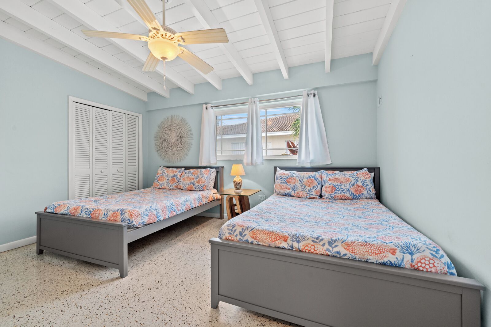 A bedroom with two beds, a ceiling fan, a window with curtains, and a wall decoration.