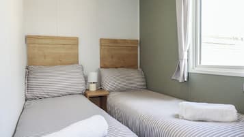 A room with two single beds, a nightstand with a lamp, and a window with a curtain.