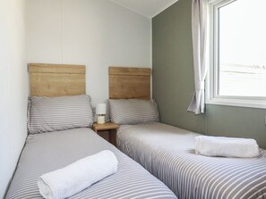 Ein Zimmer mit zwei Einzelbetten, einem Nachttisch mit Lampe und einem Fenster mit Vorhang.