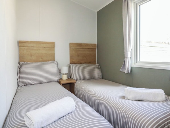 A room with two single beds, a nightstand with a lamp, and a window with a curtain.