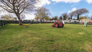 A playground with swings, a red tractor, and a fenced area. - Shamrocks Cove Caravan (Newquay)