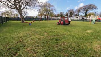 A playground with swings, a red tractor, and a fenced area.