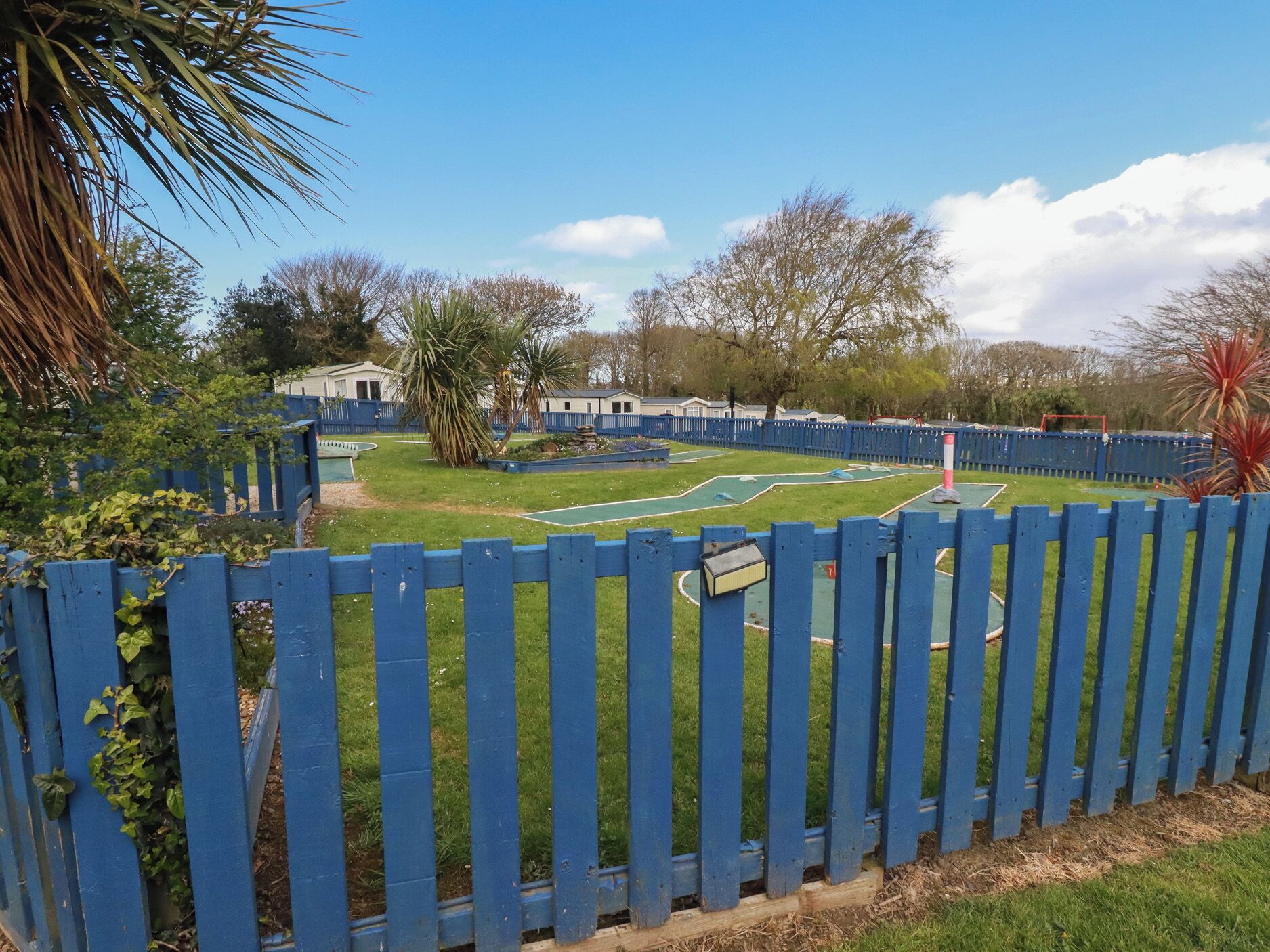 A fenced outdoor area with a green lawn, a small pool, and a tennis court.