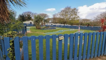 A fenced outdoor area with a green lawn, a small pool, and a tennis court.