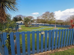 A fenced outdoor area with a green lawn, a small pool, and a tennis court.