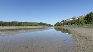 A river with calm water reflecting the sky, surrounded by green hills and a building on the right.
