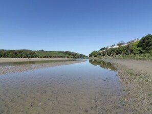 A river with calm water reflecting the sky, surrounded by green hills and a building on the right.
