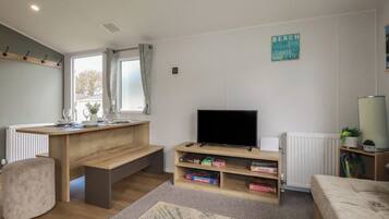 A living room with a TV, bookshelf, and a window with curtains.