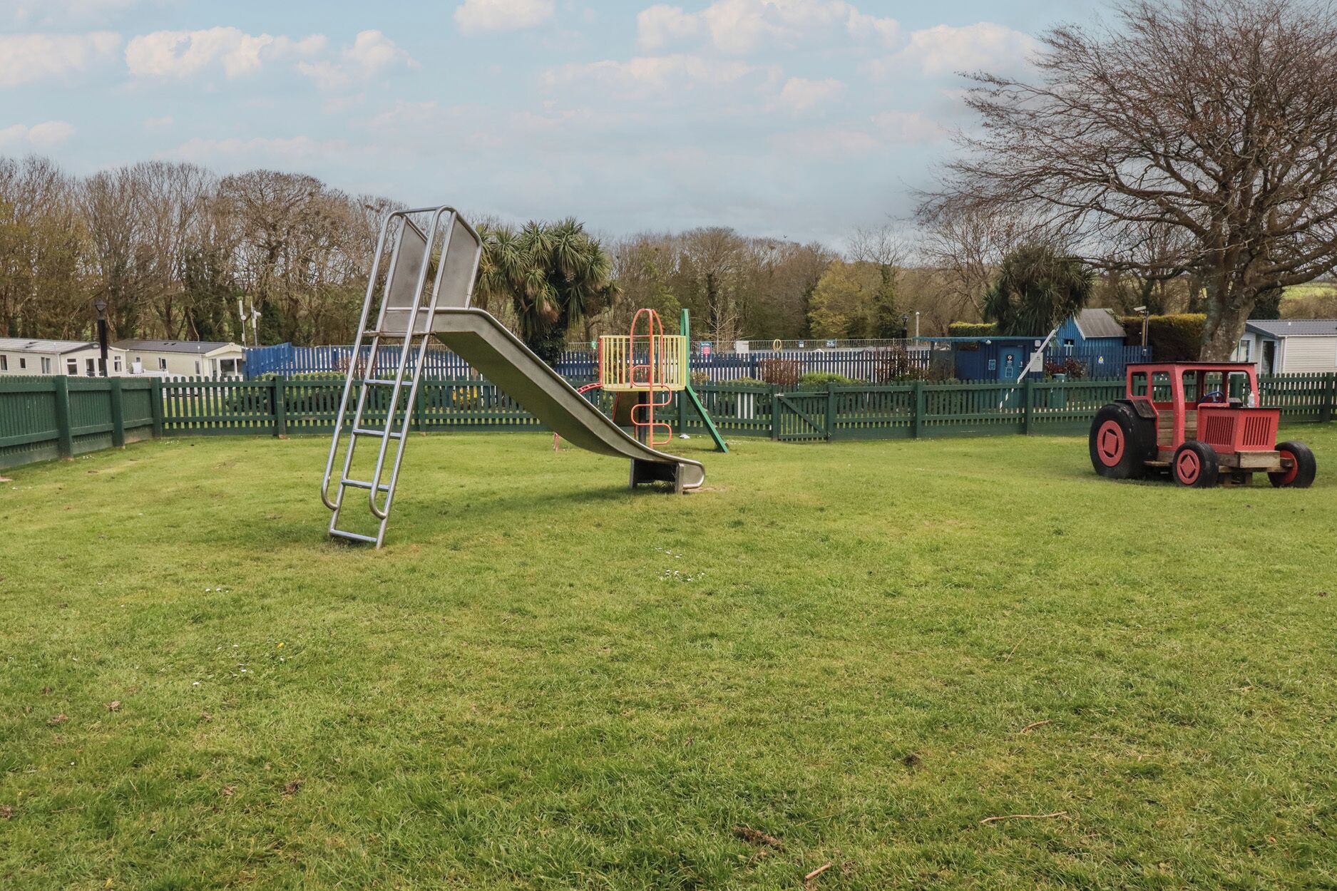 A playground with a slide, a ladder, and a red tractor in a grassy field.