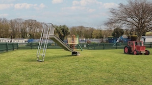 A playground with a slide, a ladder, and a red tractor in a grassy field. - Shamrocks Cove Caravan (Newquay)