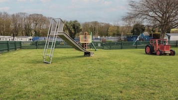 A playground with a slide, a ladder, and a red tractor in a grassy field.