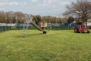 A playground with a slide, a ladder, and a red tractor in a grassy field.