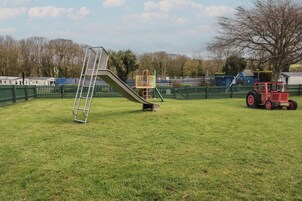 Un parque infantil con un tobogán, una escalera y un tractor rojo en un campo cubierto de hierba.