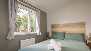 Un dormitorio con cama, ropa de cama verde, cabecera de madera, ventana con cortinas y un radiador.
