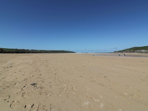 Ein weiter, sandiger Strand mit Fußspuren, ein klarer, blauer Himmel und ferne Hügel.