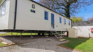 A mobile home with a ramp leading to the entrance, a small attached utility shed, and a gravel driveway.