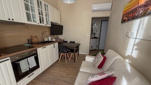 Una cucina moderna con mobili bianchi, un'area pranzo con tavolo e sedie, e un divano in pelle bianca con cuscini decorativi.
