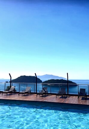 Ein Poolbereich mit Liegestühlen und Blick auf das Meer und eine entfernte Insel.