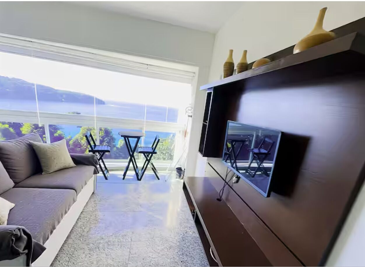 Una sala de estar moderna con un sofá, un televisor montado en la pared y un balcón con vistas.