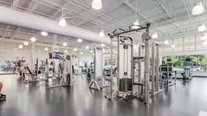 Une salle de sport équipée de divers appareils d’exercice, dotée d’un grand miroir et d’un plafond haut avec un éclairage industriel.