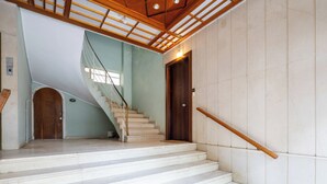 Eine Treppe mit einem hölzernen Geländer, einer hellgrünen Wand und einer dunklen Holztür am Oberende.