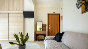Ein modernes Zimmer mit einer Couch, einem kleinen Tisch mit Topfpflanze, einem Holztisch mit Spiegel und einem Kleiderschrank.