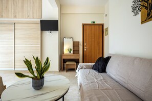 A modern room with a sofa, a small table with a potted plant, a wooden desk with a mirror, and a wardrobe. - Artemis Coast Stays II - modern cozy apartment, 300 meters from the beach! (Artemis)