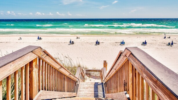 Ein Strand mit hölzernen Stegen, die zum Ufer führen, bewölkter, klarer Himmel und Meereswellen.