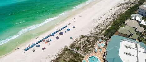 An aerial view of a beach resort with a swimming pool, beach umbrellas, and a beach area.
