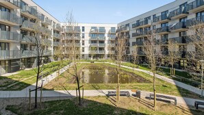 Un moderno complejo de apartamentos con varios balcones, un patio central con un estanque y un césped bien cuidado.