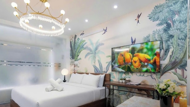 Habitación de hotel con cama, televisión, candelabro y un mural en la pared.
