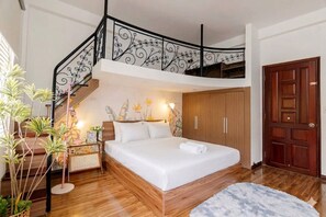 Un dormitorio con cama, mesita de noche, cómoda, escalera de madera y una puerta.