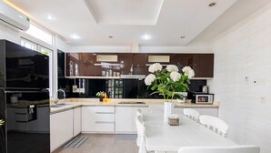 Una cocina moderna con armarios blancos, un refrigerador negro, una mesa de comedor con sillas blancas y un florero con flores en la encimera.