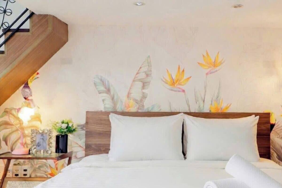 Ein Schlafzimmer mit einem Bett, Kissen, einem Nachttisch, einer Lampe und einer Wand mit floralen Bildern.