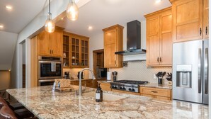Eine Küche mit Granit Arbeitsplatten, Edelstahlgeräten, Holzschränken und Pendelleuchten.