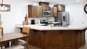 Une cuisine moderne dotée de meubles en bois, d’appareils électroménagers en acier inoxydable, d’un îlot central et d’un éclairage encastré au plafond.