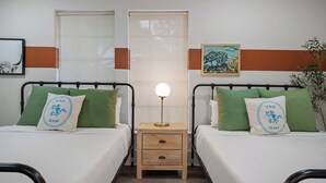 Une chambre double avec deux lits, une table de chevet avec une lampe et une fenêtre avec des stores.