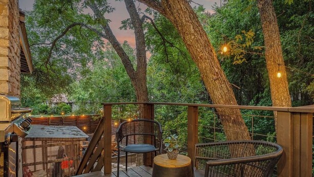 Une terrasse en bois, agrémentée de chaises et d’une table, entourée d’arbres et illuminée de guirlandes lumineuses.