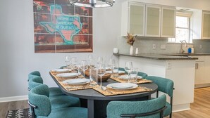 Un coin repas avec une table ronde dressée pour six personnes, des chaises de couleur turquoise et une cuisine en arrière-plan.