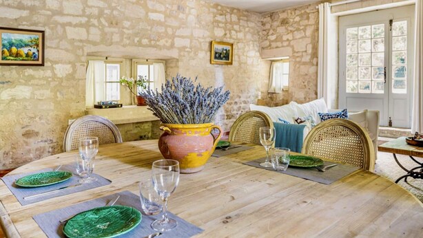 A rustic dining room with a stone wall, wooden table, and wicker chairs. - Cosy house in Provence Swimming pool & park 4 people (Beaucaire)