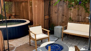 Ein Garten mit Whirlpool, Holzstühlen, einer Feuerstelle und einem überdachten Sitzbereich.