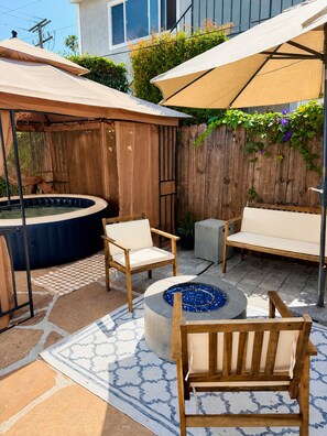 Ein Garten mit Whirlpool, Holzstühlen, einer Feuerstelle und einem überdachten Sitzbereich.