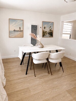 Un comedor con una mesa redonda, sillas blancas y dos cuadros en la pared.