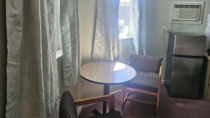 A small room with a round table and two chairs, a refrigerator, and a window with curtains.