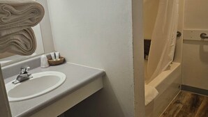 A bathroom with a white sink, a mirror, a shower curtain, and a wooden floor.
