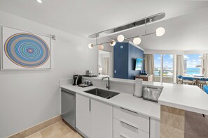 A modern kitchen with a central island, a dishwasher, and a large window overlooking a balcony. - Fontainebleau Tresor 1 BDRM Ocean + Pool View (Miami Beach)