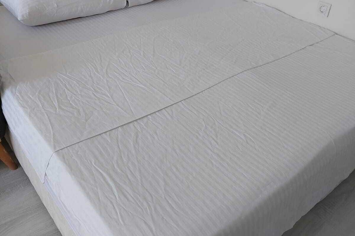 A bed with white bedding, a wooden headboard, and a white wall.
